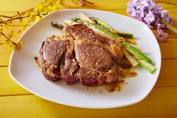 Appetizing rib eye steak served with asparagus on table