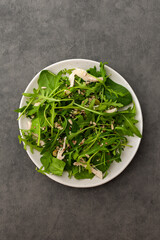 Delicious light salad with arugula and chicken breast sprinkled with various healthy seeds in a plate on a gray background, top view