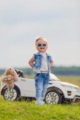 girl in sunglasses stands in front of a white children's car
