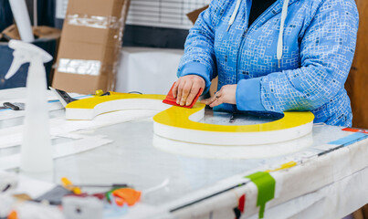 Applying colored yellow membrane to a surface of plastic 3d letter of signboard. Worker's hands...