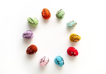 Crochet colored Easter eggs arranged in a circle on a white background. Top view.