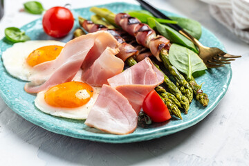 Ketogenic diet. Keto brunch breakfast. fried eggs, asparagus wrapped in bacon, ham, tomatoes and salad. Food recipe background. Close up