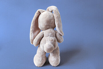 long-eared bunny stands turned away, the back of a soft toy on a bright blue background