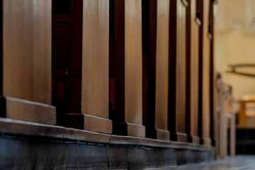 Fototapeta na wymiar Selective focus the side of bench in the church between corridor with the sunlight, Inside the building with a row and lines of brown wooden pews in catholic church or chapel.