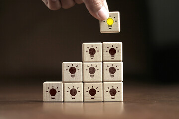 Concept, creativity and innovation. Hand flip the wooden cube block with illuminated light bulb icon placed on the wooden block, the dark light bulb icon stacked up.