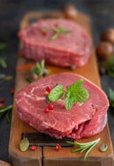 Raw beef fillet steaks with herbs and spices on wooden board on dark background close up