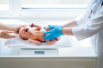 New born baby girl on a scale. Female doctor weighting cute baby in clinic.