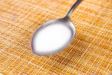 table spoon with white liquid of milk on a light brown clipped background, kitchen food and drink concept