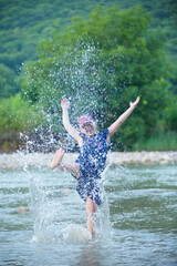 The girl is standing by a small clear mountain river. Splashes from playing with water.