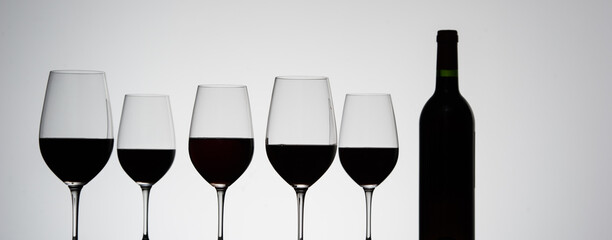  Glasses with red grape wine and a bottle on a white glossy surface. High quality photo