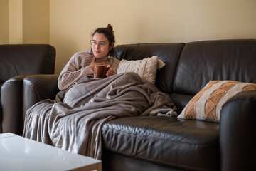 Obraz premium Ill woman resting on the couch with a cup of tea.