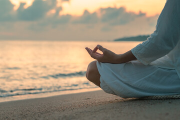 Close up woman in white clothes and a turban sits by the sea on a sandy beach at dawn on a summer...