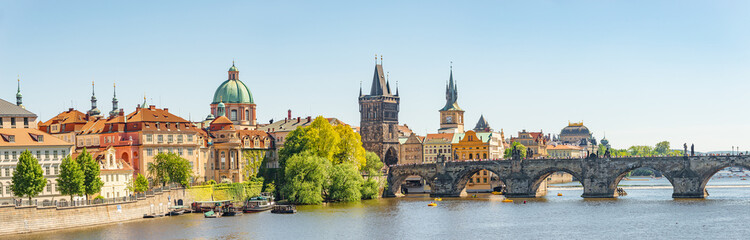 Panoramic view over magnificent Vltava river with tour boats, tourists and famous Charles Bridge and walking embarkment in historical downtown of Prague, Czech Republic at blue sunset summer sky.