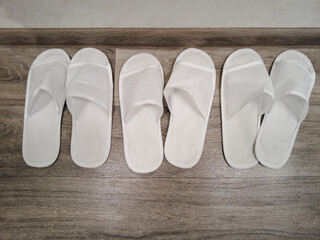Three pairs of white disposable slippers in a hotel on a brown wooden floor