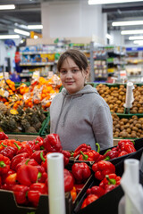 Young positive teen girl consumer  at grocery section of supermarket