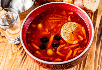 Solyanka soup with meat, sausage, vegetables, olives and lemon in bowl on wooden table background