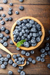 Freshly picked blueberries in a wooden bowl and spoon. Berries are scattered on a wooden table. Healthy berry, organic food, antioxidant, vitamin
