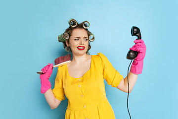 Comic portrait of young emotional girl, housewife with curlers on her head isolated on blue studio...