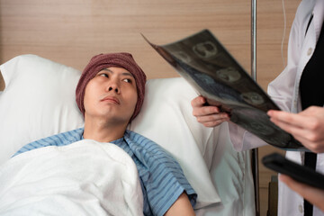 Selective focus of a depressed Asian male cancer patient in a head cover laying on bed looking at a...