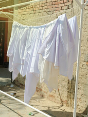 Clean bedsheet hanging on a clothesline at the street. White and soft bedding sheet against old wall