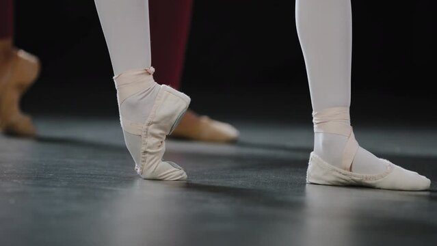 Two pairs of female legs on floor on performance stage in dance class studio do ballet exercises stretching the feet stand on pointe shoes ballerinas dance girl repeats movements of teacher trainer