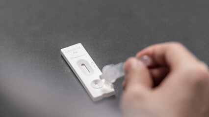 A hand dripping the extraction liquid on the cassette of a rapid antigen test 