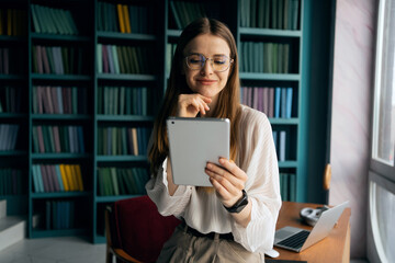 The receptionist is a woman with glasses working in a modern office using a laptop computer,...