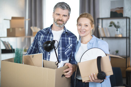Close up of Caucasian couple smiling and hugging at new flat holding cardboxes with home decorations. Family preparing to moving to modern apartment.