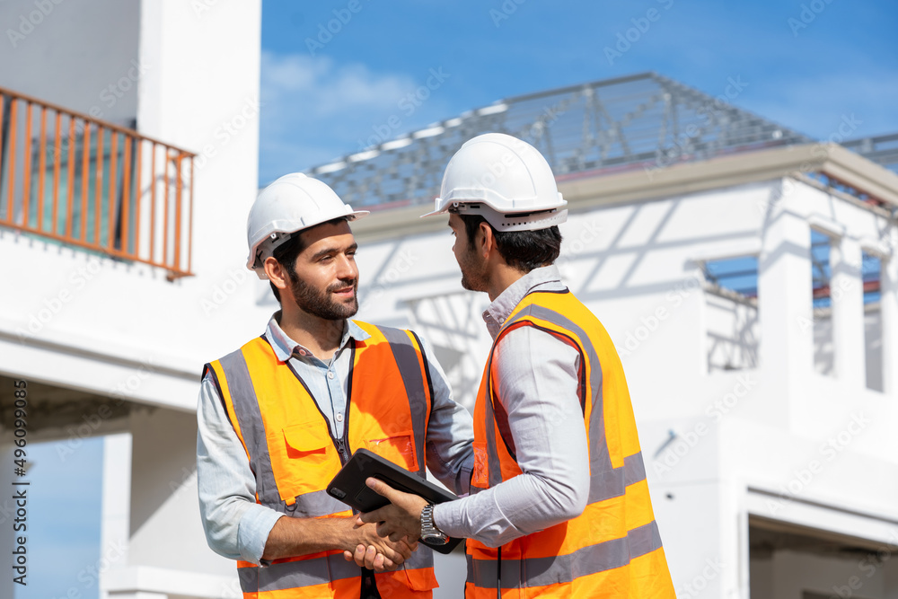 Poster Engineer and architect in protective helmets and vests are shaking hands while working in construction site.