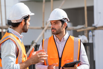 Professional architects in safety vests at a construction site while discussing their work plan at...