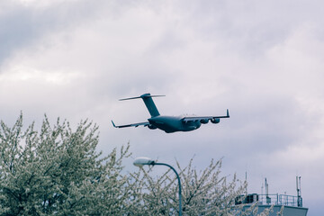 Big grey plane taking off from airport. Control tower in a flowering trees - obrazy, fototapety, plakaty