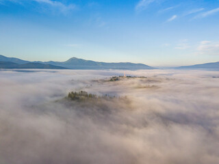 Flight over fog in Ukrainian Carpathians in summer. A thick layer of fog covers the mountains with a solid carpet. Mountains on the horizon. Aerial drone view.