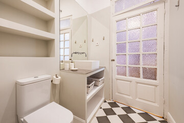 Fototapeta na wymiar Toilet with built-in washbasin cabinet with white porcelain sink, wooden door with opaque glass and checkered tiled floors