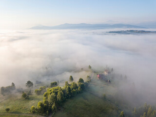 Fototapeta premium Fog envelops the mountain forest. The rays of the rising sun break through the fog. Aerial drone view.