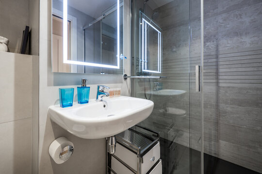 Bathroom with glass sliding door shower stall, porcelain hanging sink, integrated frameless mirror with light