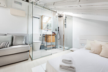 Apartment with exposed wooden beams painted white, glass cabin with bathroom with white porcelain...