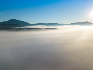 Flight over fog in Ukrainian Carpathians in summer. Mountains on the horizon. A thick layer of fog covers the mountains with a continuous carpet. Aerial drone view.