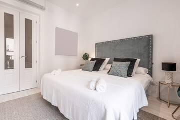 Bedroom with studded blue velvet headboard, lots of cushions on the bed and white woodwork