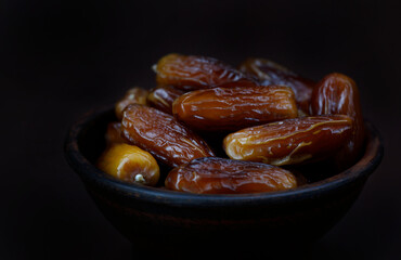 Clay bowl of ripe beautiful dates. Dried dates on a brown background.