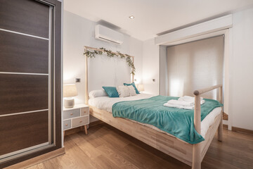 Bedroom with wooden bed with balustrades, dark wood built-in wardrobe, air conditioner and four drawer bedside tables in vacation rental apartment