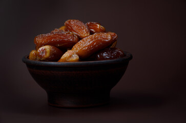 Ripe dried dates in a clay cup on a brown background.