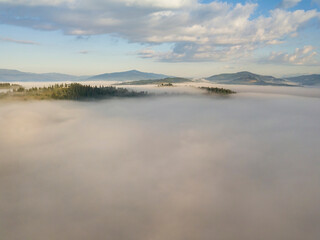 Flight over fog in Ukrainian Carpathians in summer. Mountains on the horizon. A thick layer of fog covers the mountains with a continuous carpet. Aerial drone view.