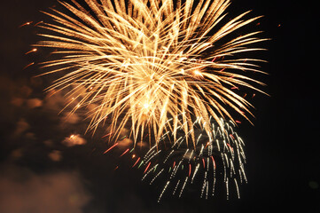 explosions of yellow round-shaped fireworks against the black night sky. The concept of a holiday,...
