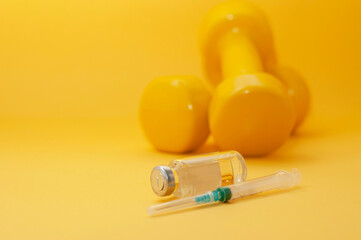 syringe and a jar of liquid lie in front of the dumbbells on a yellow background, copy space, close-up. the concept of doping in sports, steroids, testosterone and other drugs banned in sports.