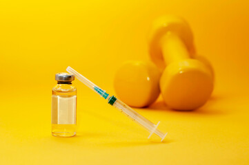 syringe and a jar of liquid stand next to dumbbells on a yellow background, a horizontal picture....