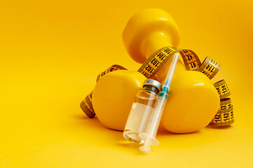 syringe and jar of liquid lie on dumbbells with a measuring tape on a yellow background, a horizontal picture. the concept of doping in sports, steroids, testosterone and other drugs for weight loss.