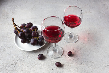 two glasses with red wine and grapes on a concrete background