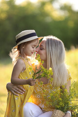 Mother and little daughter having fun in summer meadow with yellow flowers. Happy family on summer. Concept of healthy family without allergies. High quality photo