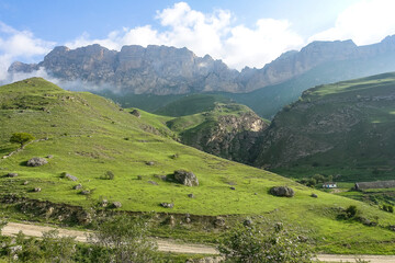 Fototapeta premium The landscape of the green Aktoprak pass in the Caucasus, the road and the mountains under gray clouds. Kabardino-Balkaria, Russia