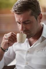 A senior businessman in casual clothes sits on the terrace of a luxury house and drinks morning coffee. Selective focus 